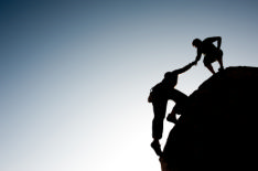 The photo shows a couple helping each other to reach the top of a cliff, a metaphor for achieving their goal of getting a job.
